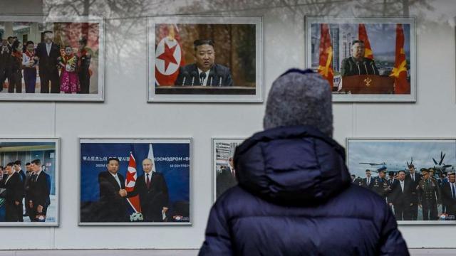 一名身穿蓝色羽绒外套、头戴灰色帽子的男子透过窗户观看朝鲜领导人金正恩的照片。