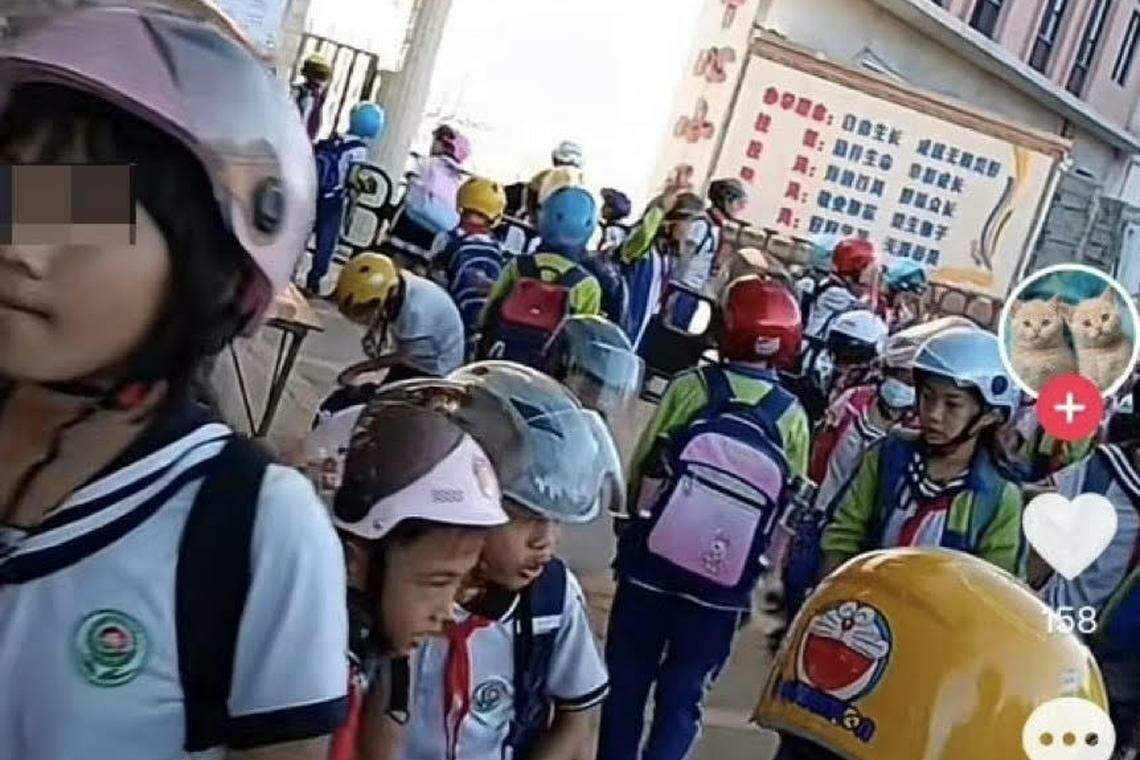 广东省湛江市徐闻县的角尾乡中心小学门口,上学生们无论走路还是坐车都戴着头盔。(视频截图)