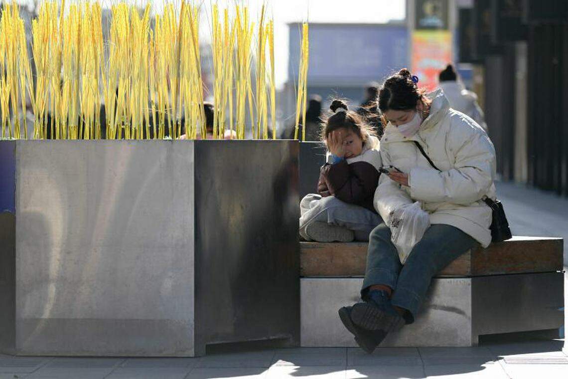 中国媒体曾在2021年发文形容网络游戏为“精神鸦片”和“电子毒品”。图为北京一名孩子12月2日在街道长凳上休息时,看着一名正在使用手机的妇女。(法新社)