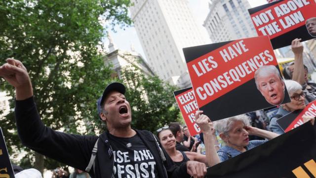 特朗普被指控在2016年大选前伪造文件,掩饰他的前律师曾向丹尼尔斯支付"封口费"(图为抗议人士举着标语牌示威)。