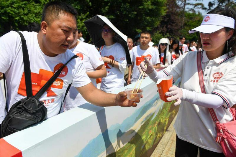 世界锅包肉大赛工作人员(右)为品鉴官夹取制作完成的锅包肉。(新华社)