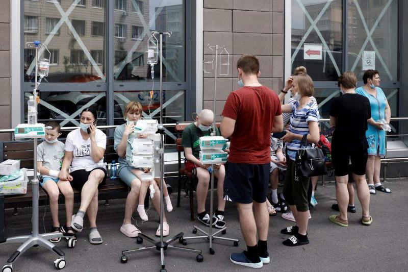 儿童医院遇袭后,一些伤患和病患带着输液架坐在医院外围,等待执法人员安排撤离。(路透社)