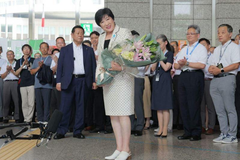 在东京都知事选举中第三次连任后,小池百合子(中)星期一(7月8日)手捧一束鲜花脸带微笑抵达东京都厅大楼。(法新社)