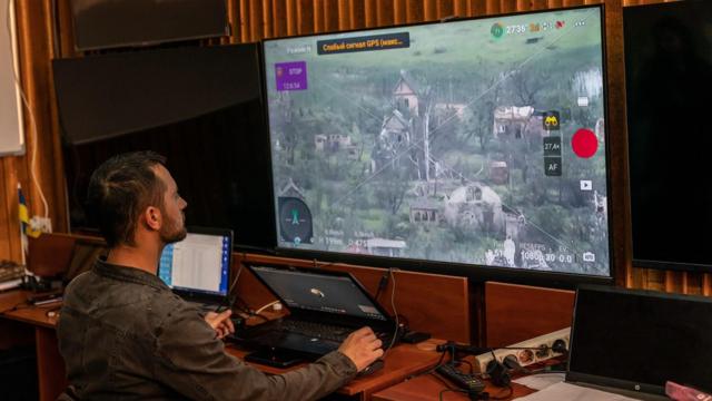 一名乌克兰无人机飞行员坐在屏幕前,屏幕上显示一架无人机飞越乌克兰东部一个村庄的图传影像,据报当地有俄罗斯军队驻扎。