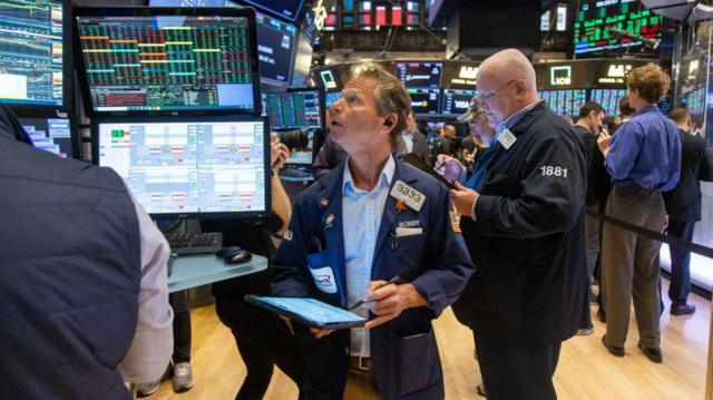 纽约证券交易所内,一名手持笔和笔记本的男子正抬头看着显示价格的电脑萤幕。(06/11/2024)