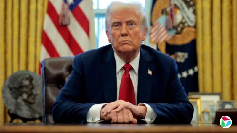 特朗普坐在椭圆形办公室的办公桌前,他穿着蓝色西装,系着红色领带