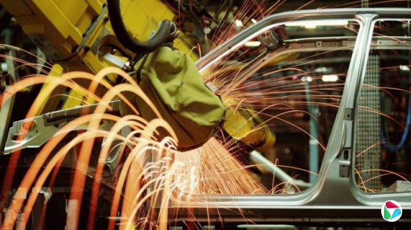 一辆正在制造中的汽车。黄色机械手臂正在加工汽车底盘,产生数十道橘红色火花。