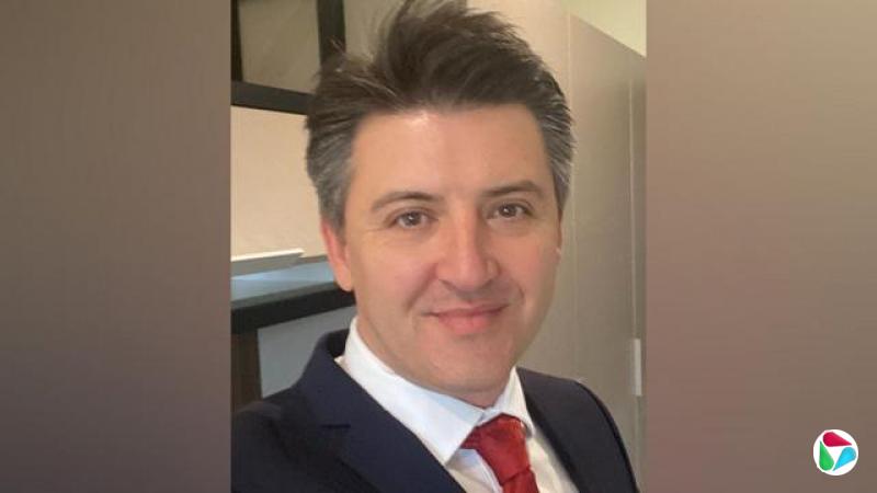 佐尼身穿深色西装,并且微笑望向镜头。