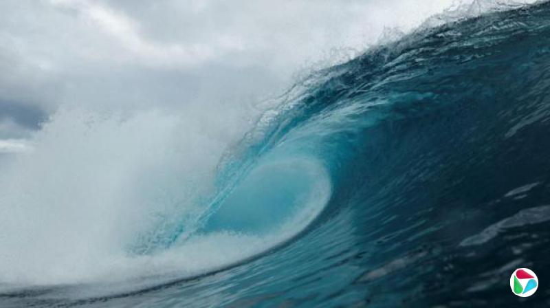 一道波浪的弧形正翻涌而上。波浪呈深蓝色,越接近波峰颜色越浅,并有白色浪花从波浪中飞溅而出。天空则布满云层。