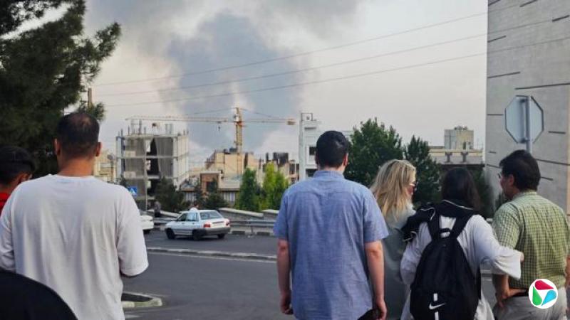 周一,在德黑兰,人们背对镜头站立,望向地平线上升起的浓烟