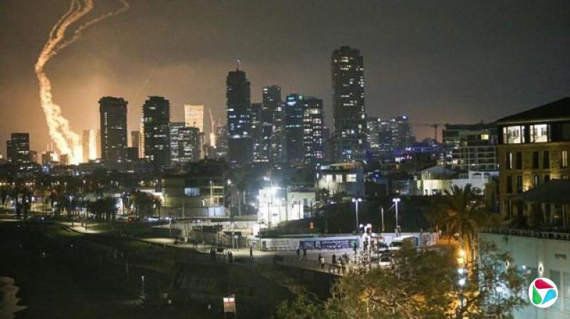 以色列特拉维夫的夜空中,有导弹划过天空的烟雾,远处地面的爆炸造成的火光。