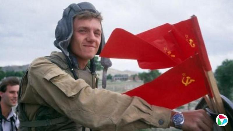 一名年轻的苏联士兵在阿富汗微笑着与红色苏联国旗合影