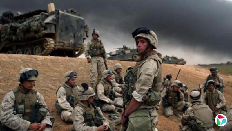 2003年4月,全副武装的美国士兵坐在沙丘上,旁边有一辆坦克,天空阴暗,准备在巴格达附近部署