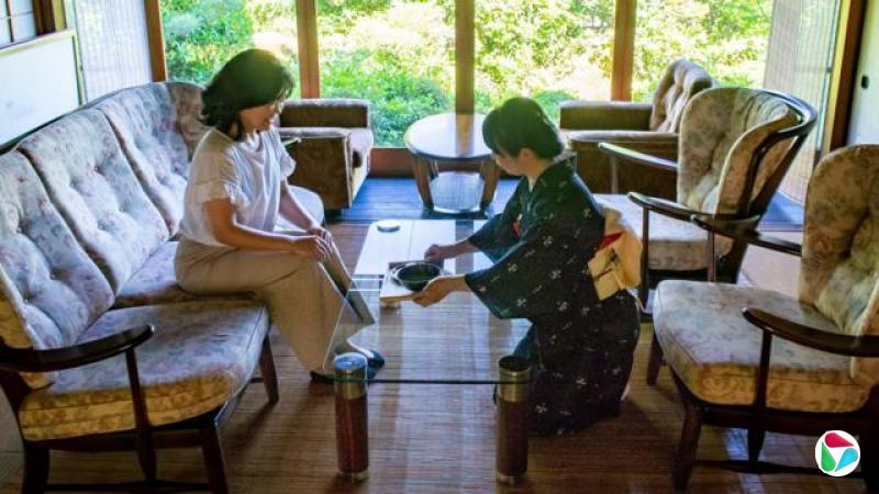 日本传统茶道的照片,左边一位身着和服的女士坐在沙发上,主人正在为她倒一杯抹茶。
