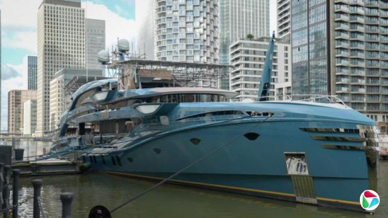 一艘大型蓝色超级游艇停泊在现代摩天大楼前
