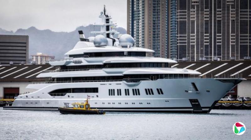 一艘巨大的白色超级游艇停泊在港口,一艘小得多的黄色船只从它前方驶过