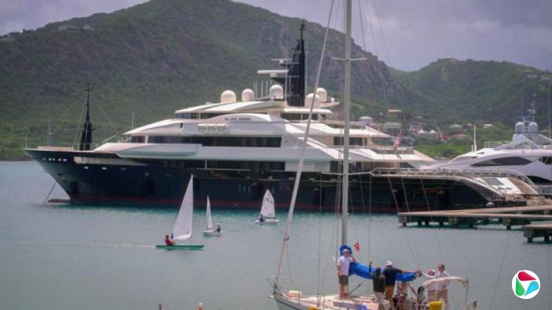 一艘蓝白相间的超级游艇停泊在港口,背景是连绵的山丘