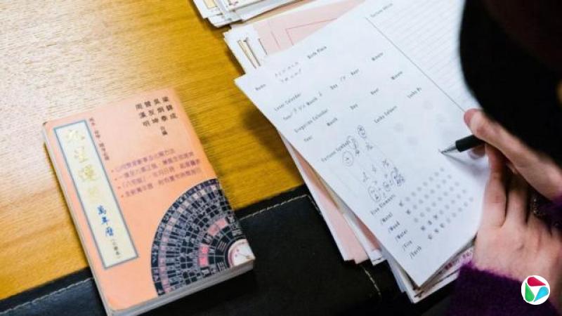 这张照片拍摄于香港一名风水师的办公室,她正在为美国总统特朗普撰写猪年运势的星盘。画面特写显示她的双手在文件和书本堆上绘制图表。