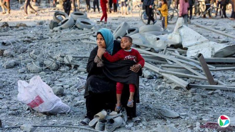 一名妇女带着儿童坐在灰色废墟中,若有所思。