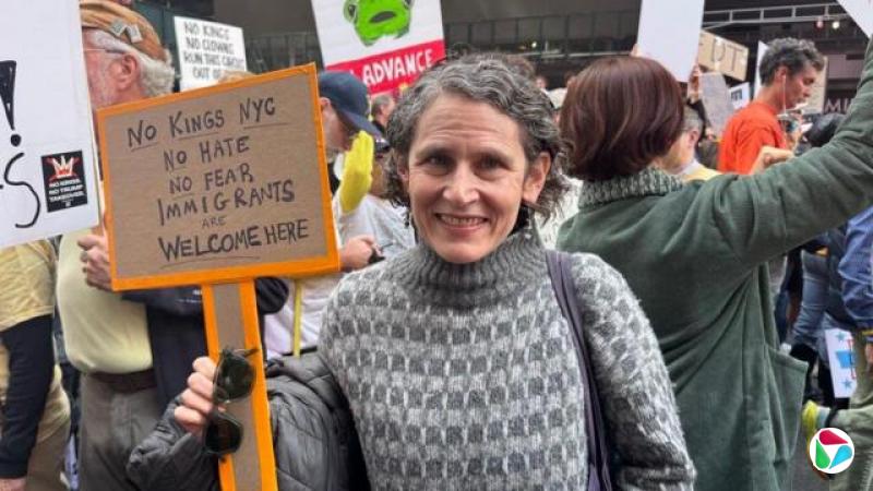 贝丝·扎斯洛夫在抗议人群前对着镜头微笑,举着一块牌子,上面写着“纽约没有国王,没有仇恨,没有恐惧,欢迎移民”