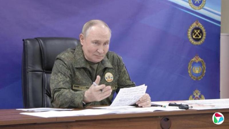 普京身穿军服,一边发言,一边手持报纸