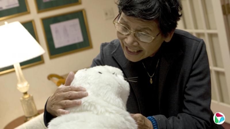 一人正在和外形像小海豹的机器人Paro说话