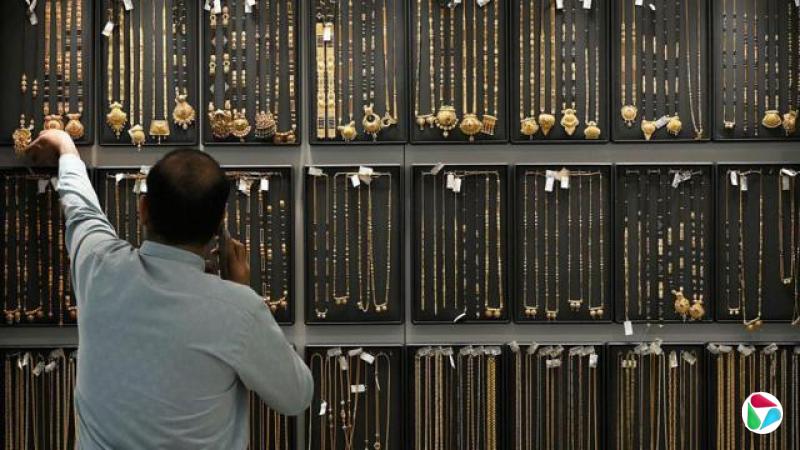 一名男子手持电话,背后展示着大量的金器。