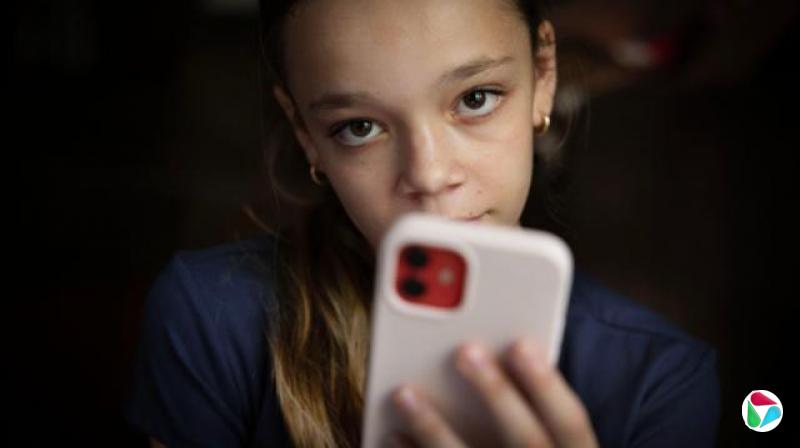 一名身穿海军蓝上衣的青少年望向镜头,粉红色手机部分遮住她的脸